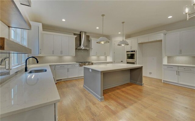 kitchen with wall chimney exhaust hood, a kitchen island, white cabinetry, and sink