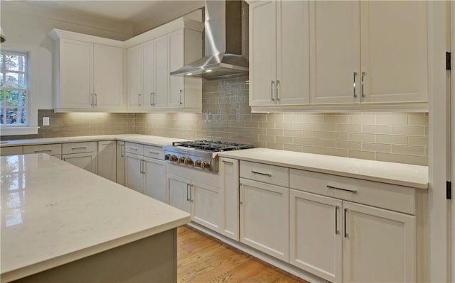 kitchen featuring wall chimney exhaust hood, stainless steel gas cooktop, tasteful backsplash, light hardwood / wood-style floors, and white cabinets