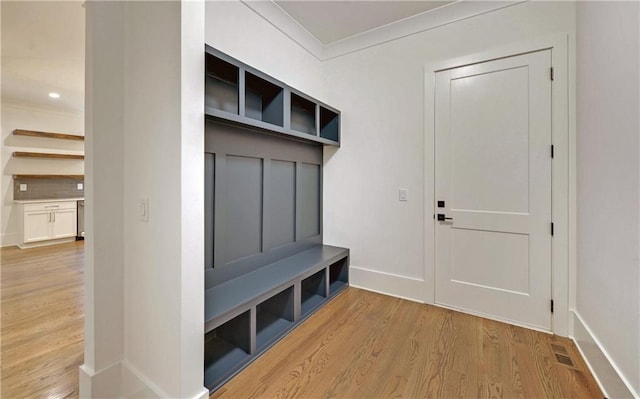 mudroom with light hardwood / wood-style flooring, built in desk, and ornamental molding