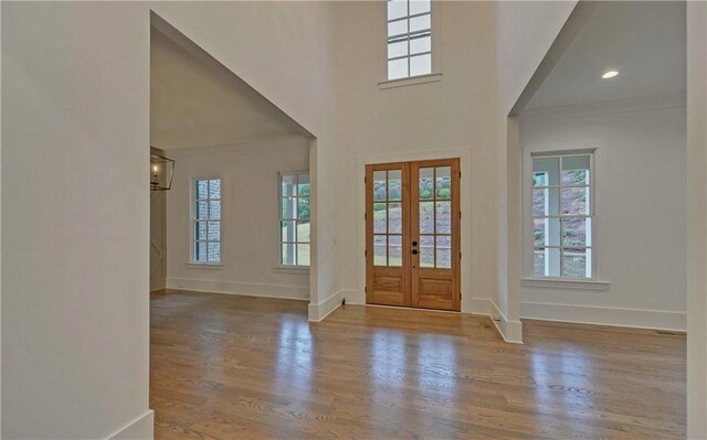 entrance foyer with french doors, a towering ceiling, and light hardwood / wood-style flooring