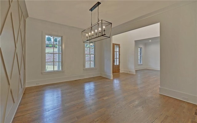 unfurnished dining area featuring wood-type flooring, crown molding, and an inviting chandelier