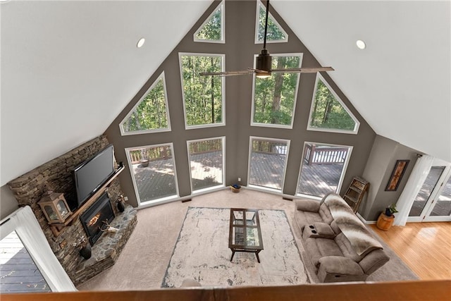 unfurnished living room with hardwood / wood-style flooring, ceiling fan, a stone fireplace, and high vaulted ceiling