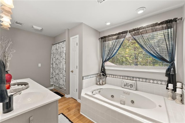 bathroom featuring hardwood / wood-style floors, vanity, and a relaxing tiled tub