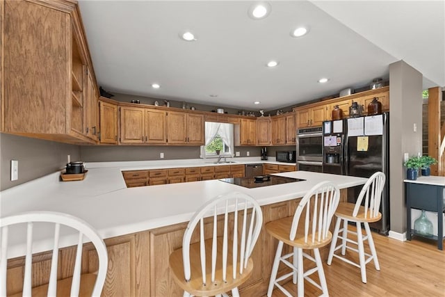 kitchen with sink, a breakfast bar, black appliances, kitchen peninsula, and light wood-type flooring