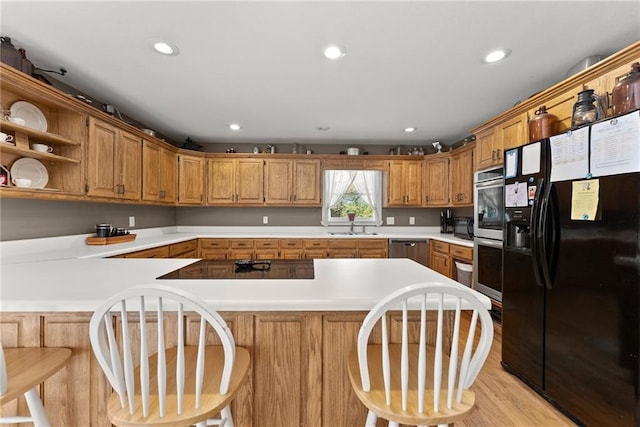 kitchen featuring a kitchen bar, sink, light wood-type flooring, kitchen peninsula, and black appliances