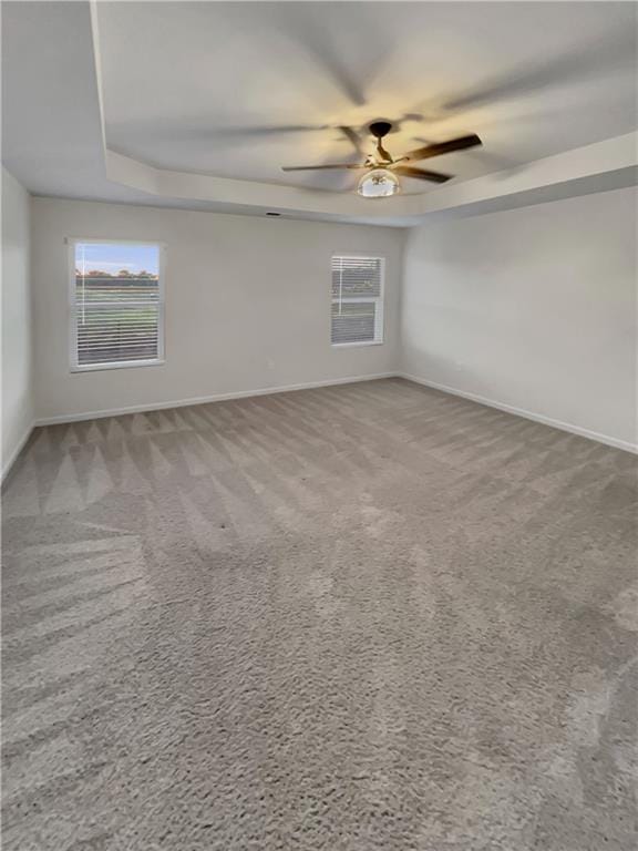 carpeted spare room featuring a tray ceiling, ceiling fan, and a healthy amount of sunlight