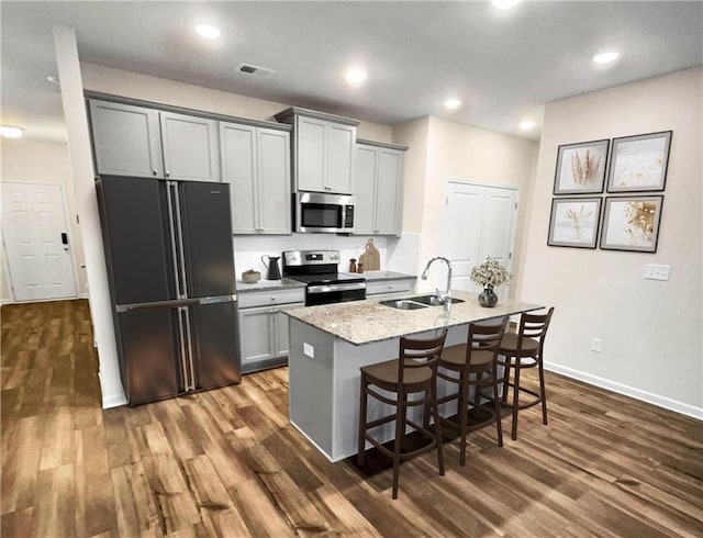 kitchen with a kitchen bar, gray cabinetry, a kitchen island with sink, and stainless steel appliances