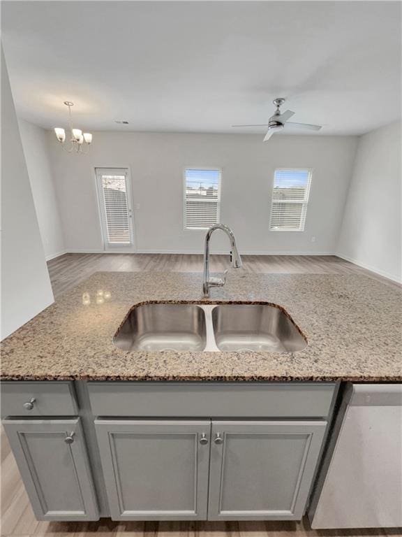 kitchen with light stone countertops, sink, dishwasher, ceiling fan with notable chandelier, and light wood-type flooring