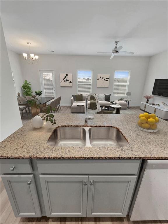 kitchen featuring dishwasher, light stone countertops, sink, and ceiling fan with notable chandelier