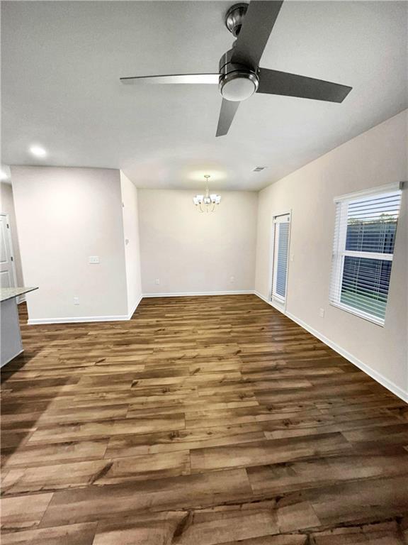 unfurnished living room with ceiling fan with notable chandelier and dark hardwood / wood-style floors