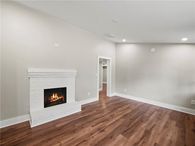 unfurnished living room with a brick fireplace, wood finished floors, and baseboards