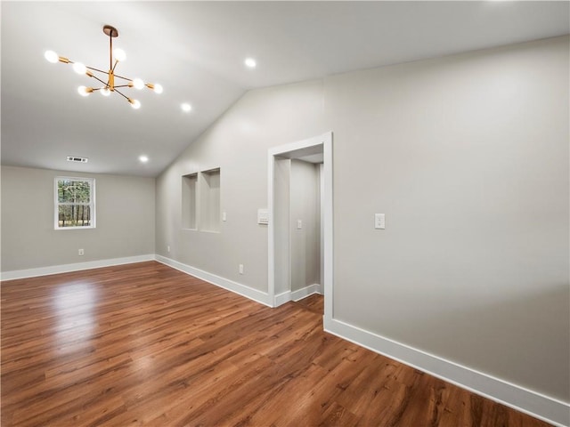 empty room with a notable chandelier, dark wood-style flooring, visible vents, baseboards, and vaulted ceiling