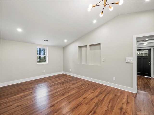 empty room with lofted ceiling, visible vents, an inviting chandelier, dark wood-type flooring, and baseboards