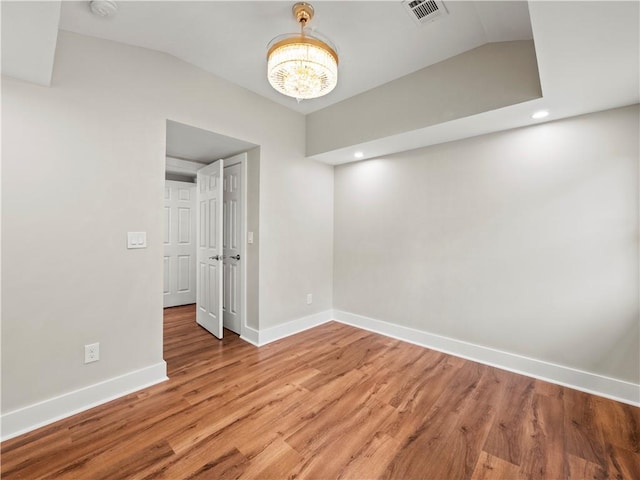 unfurnished room featuring a notable chandelier, light wood finished floors, lofted ceiling, visible vents, and baseboards