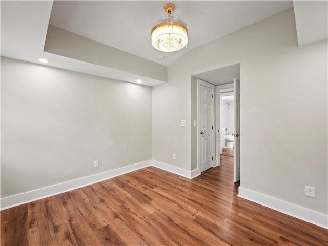 empty room featuring recessed lighting, an inviting chandelier, vaulted ceiling, wood finished floors, and baseboards