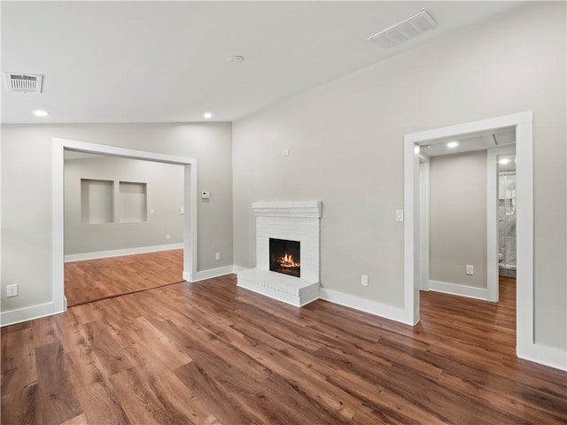 unfurnished living room with dark wood-type flooring, a fireplace, and visible vents