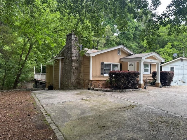 view of front of home with stone siding, concrete driveway, a chimney, and covered porch