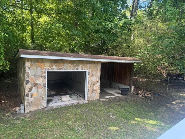 view of outbuilding with fence, a garage, an outdoor structure, and a view of trees