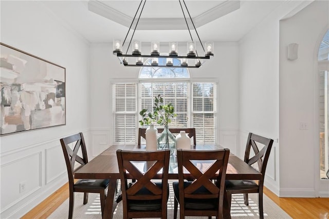 dining area featuring an inviting chandelier, a raised ceiling, and light hardwood / wood-style flooring