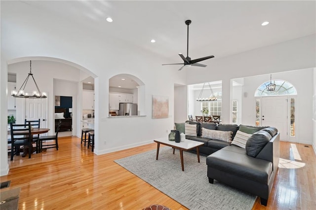 living room featuring a towering ceiling, ceiling fan with notable chandelier, and light wood-type flooring