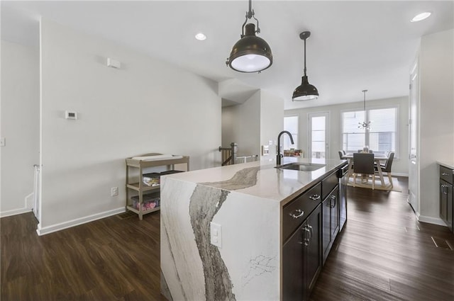 kitchen featuring dark wood-type flooring, a sink, decorative light fixtures, light stone counters, and stainless steel dishwasher