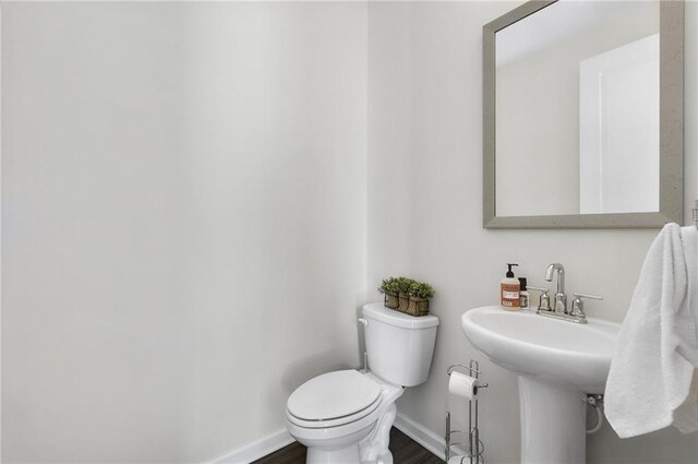 half bath featuring toilet, wood finished floors, baseboards, and a sink
