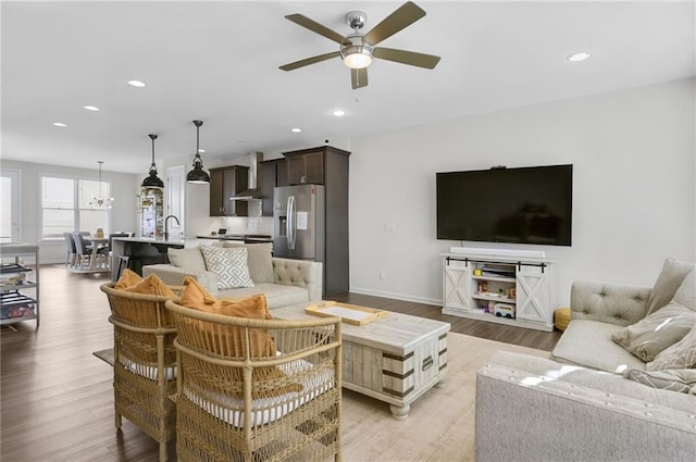 living room featuring recessed lighting, baseboards, light wood-style flooring, and ceiling fan with notable chandelier