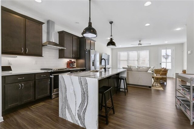 kitchen with backsplash, dark wood finished floors, a breakfast bar area, appliances with stainless steel finishes, and wall chimney exhaust hood