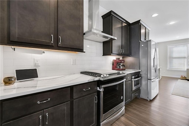 kitchen with dark wood-type flooring, light stone counters, tasteful backsplash, stainless steel appliances, and wall chimney range hood