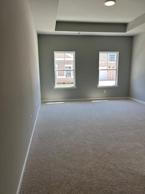 empty room featuring a tray ceiling, carpet floors, and baseboards