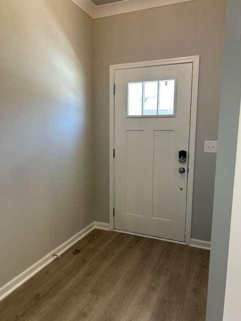 doorway featuring dark wood-style flooring, baseboards, and ornamental molding