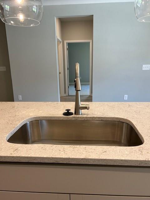 kitchen view of a sink, light stone counters, and pendant lighting