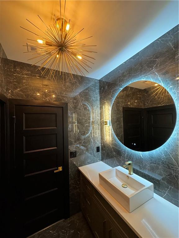 bathroom featuring backsplash, a chandelier, sink, and tile walls