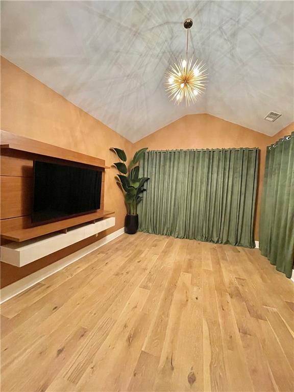 unfurnished living room with hardwood / wood-style floors, an inviting chandelier, and lofted ceiling