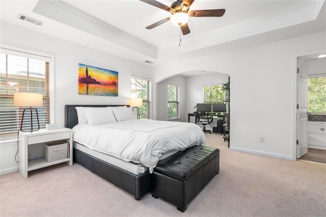 bedroom with multiple windows, ceiling fan, light colored carpet, and a raised ceiling