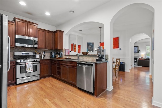 kitchen featuring backsplash, appliances with stainless steel finishes, dark stone counters, light wood-type flooring, and pendant lighting