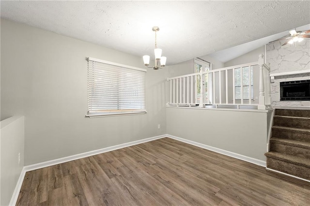 unfurnished dining area featuring a stone fireplace, a textured ceiling, vaulted ceiling, hardwood / wood-style flooring, and ceiling fan with notable chandelier