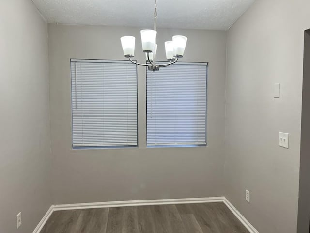 unfurnished dining area with a textured ceiling, dark hardwood / wood-style flooring, and an inviting chandelier