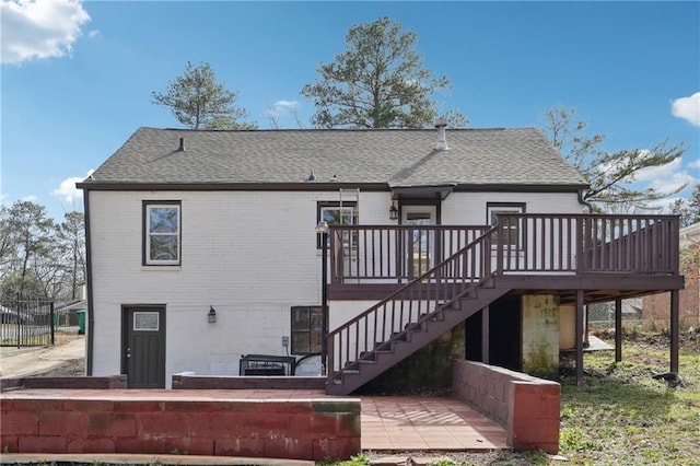 rear view of house featuring roof with shingles, stairway, a deck, and brick siding