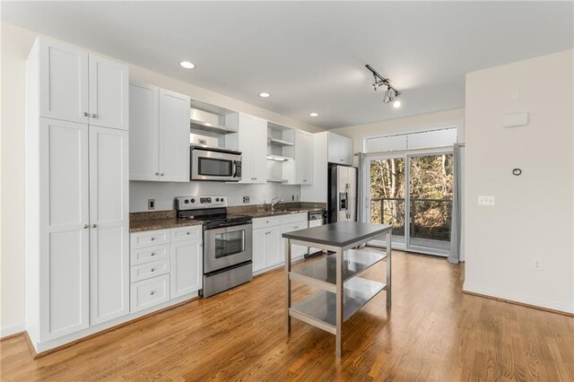 kitchen with dark brown cabinetry, stainless steel appliances, light stone countertops, and light hardwood / wood-style floors