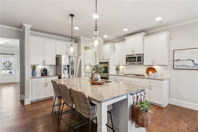 kitchen with pendant lighting, an island with sink, a breakfast bar area, white cabinets, and stainless steel appliances