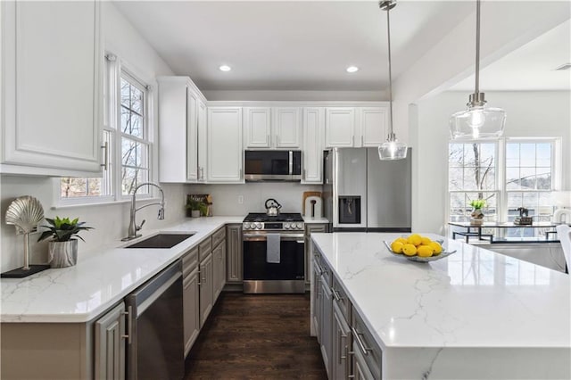 kitchen with stainless steel appliances, a kitchen island, a sink, white cabinetry, and light stone countertops