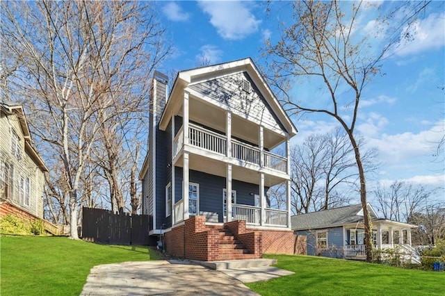 view of front facade with a balcony, a chimney, fence, and a front yard