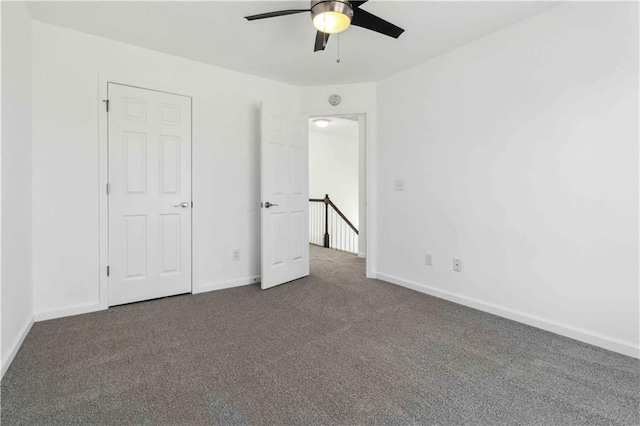 unfurnished bedroom with a ceiling fan, dark colored carpet, and baseboards