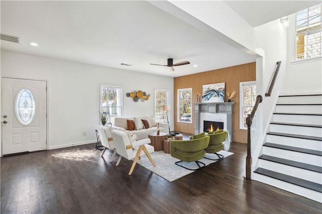 living room with a warm lit fireplace, wood finished floors, visible vents, and stairs