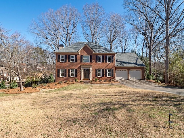 colonial inspired home featuring brick siding, a chimney, an attached garage, driveway, and a front lawn