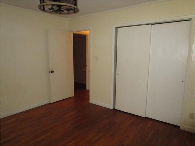 unfurnished bedroom featuring dark hardwood / wood-style flooring, crown molding, a closet, and an inviting chandelier