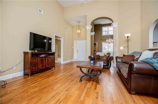 living area with baseboards, a chandelier, light wood-type flooring, a high ceiling, and arched walkways