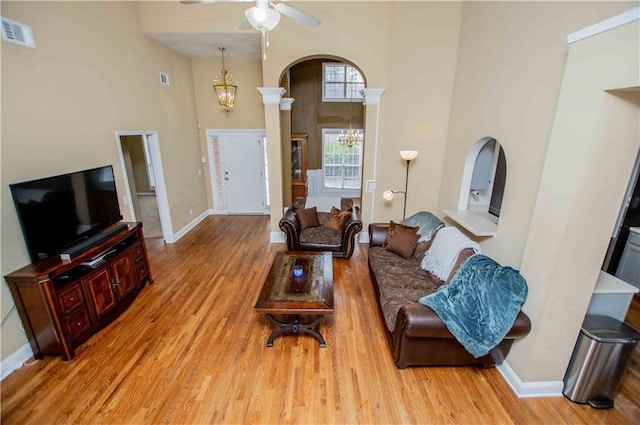 living area with visible vents, light wood finished floors, baseboards, a high ceiling, and arched walkways