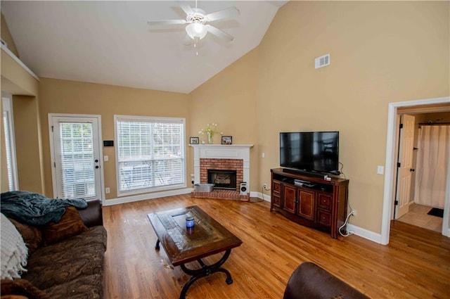 living room with visible vents, a brick fireplace, baseboards, light wood-style floors, and high vaulted ceiling